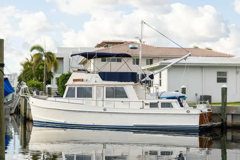 The Image of 1985 Grand Banks 42 Classic yacht docked by waterfront homes, under a partly cloudy sky. - 0