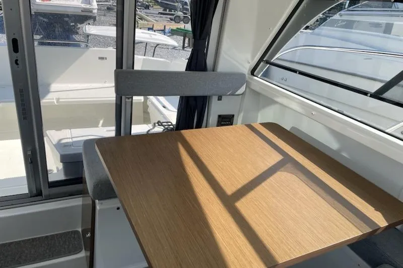 Slide: The Image of Interior of 2019 Beneteau Antares 23, featuring a wooden table and seating by large windows. - 11