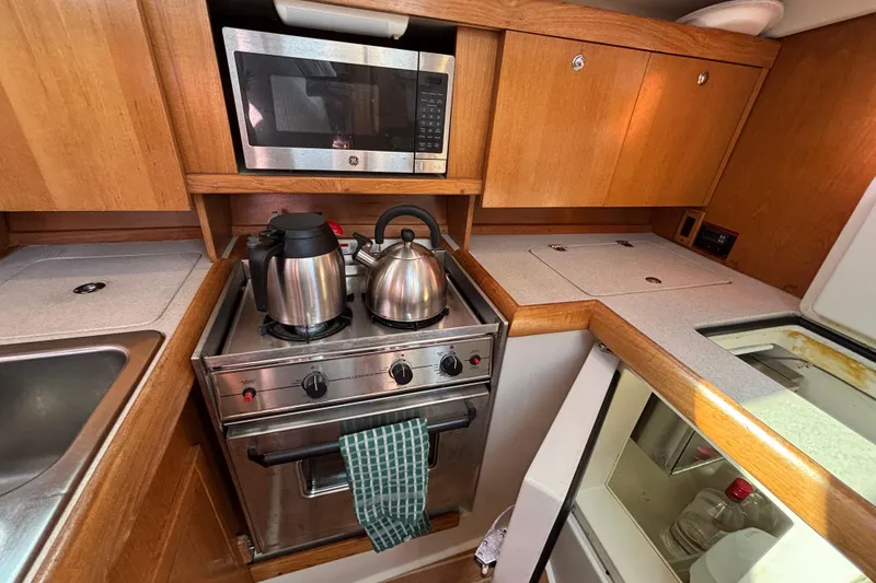 Slide: The Image of 2004 Catalina 350 yacht kitchen with stove, microwave, and wooden cabinetry. - 13