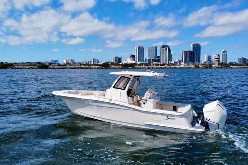 Slide: The Image of 2026 Scout 288 LXF boat cruising on water with city skyline in background. - 2