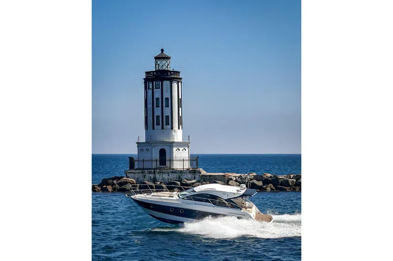 Slide: The Image of 2014 Beneteau Gran Turismo 38 yacht cruising near a lighthouse on a sunny day. - 2
