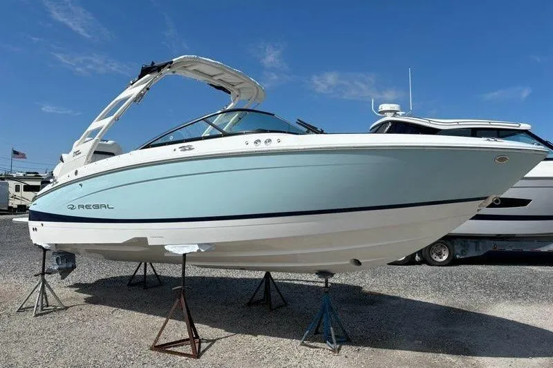 The Image of 2023 Regal LX4 boat on stands, light blue hull, clear sky background. - 0