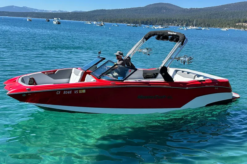 Slide: The Image of 2021 MasterCraft NXT24 boat on clear blue lake with scenic mountain backdrop. - 1
