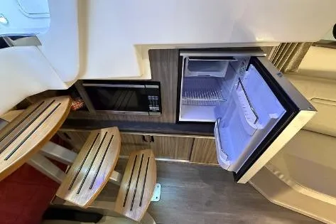 Slide: The Image of 2021 Sea Ray 320 Sundancer interior with open fridge, microwave, and wooden seating. - 5