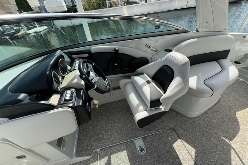 Slide: The Image of 2015 Crownline 285 SS boat interior with steering wheel and seating, docked by water. - 32