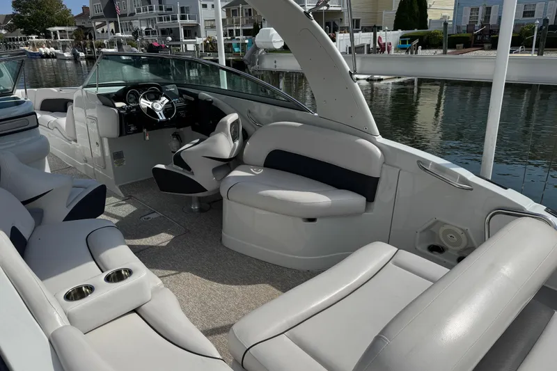 Slide: The Image of 2015 Crownline 285 SS boat interior with plush seating and steering wheel, docked by waterfront homes. - 49