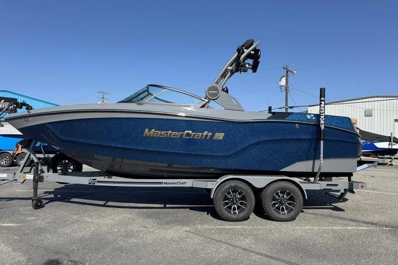 The Image of 2026 MasterCraft XT22 boat on trailer, blue exterior, parked outdoors. - 0