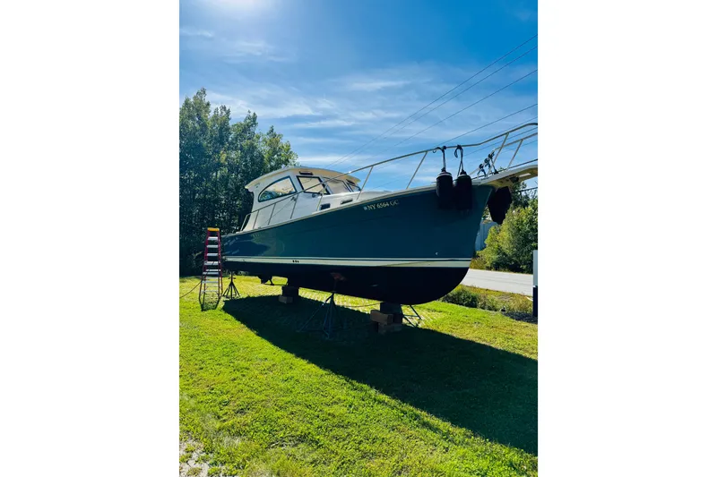 Slide: The Image of 2006 Mainship Pilot 30 Sedan boat on land, sunny day, surrounded by trees. - 32