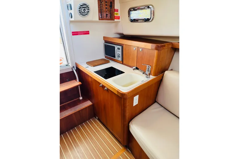 Slide: The Image of 2006 Mainship Pilot 30 Sedan interior with kitchenette, featuring sink, stove, and microwave. - 6