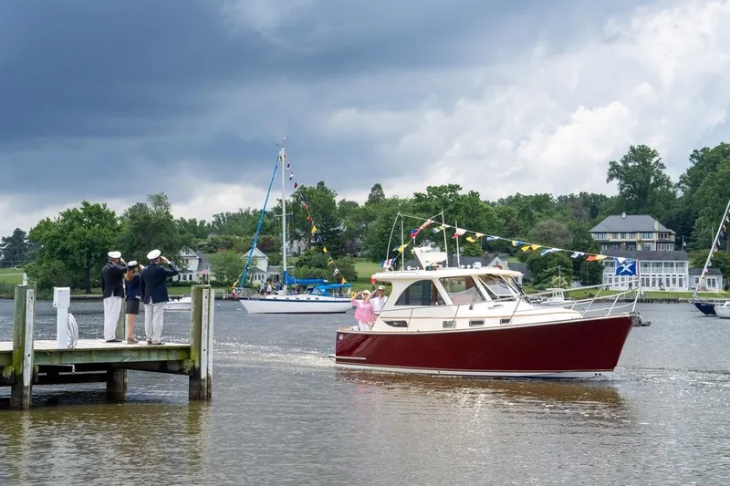Slide: The Image of 2007 Legacy Yachts 32 cruising near a dock with people saluting, under a cloudy sky. - 16