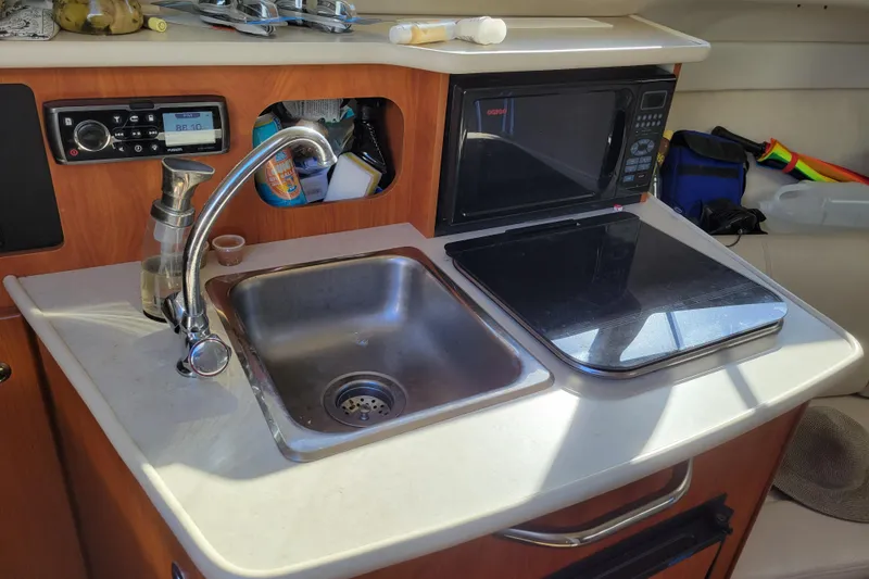 Slide: The Image of Compact kitchen area in a 2003 Bayliner 245 boat with sink, stove, and microwave. - 19