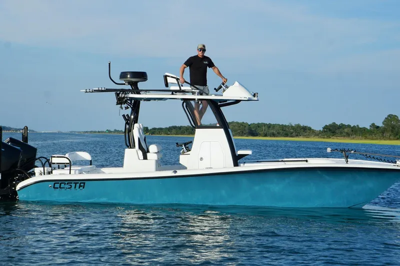 Slide: The Image of 2025 Costa Custom Boats 264 HC interior with white seating and steering wheel on water. - 14