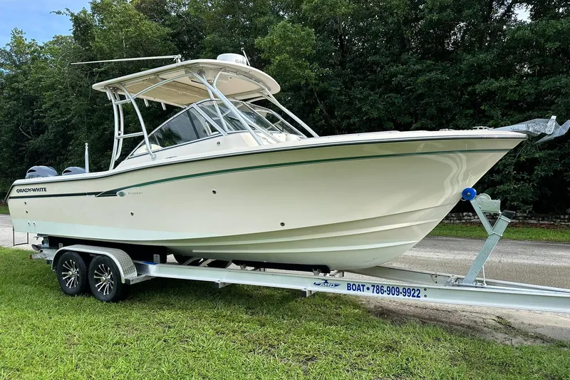 The Image of 2011 Grady-White Freedom 275 boat on trailer, parked on grass, with lush trees in background. - 1