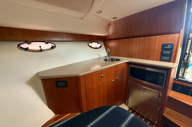 Slide: The Image of 2012 Tiara Yachts 3100 Coronet interior with kitchenette, featuring wood cabinetry and porthole windows. - 15