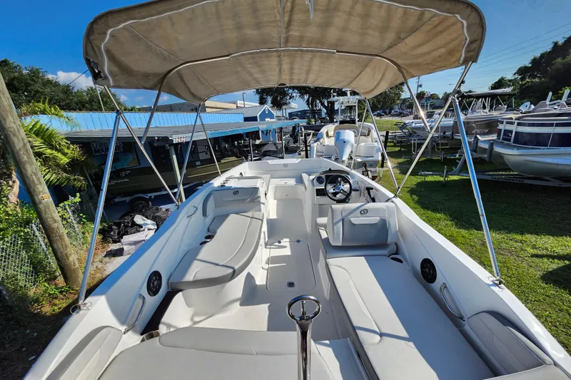 Slide: The Image of 2023 Hurricane SunDeck Sport 205 OB boat with canopy, spacious seating, and steering wheel in a marina. - 2