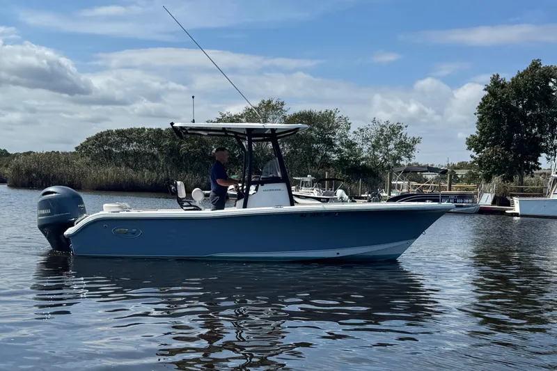 Slide: The Image of 2022 Sea Hunt Ultra 219 boat on calm water with trees in the background. - 0