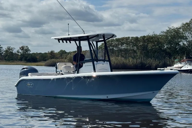 Slide: The Image of 2022 Sea Hunt Ultra 219 boat on calm water with trees in the background. - 15