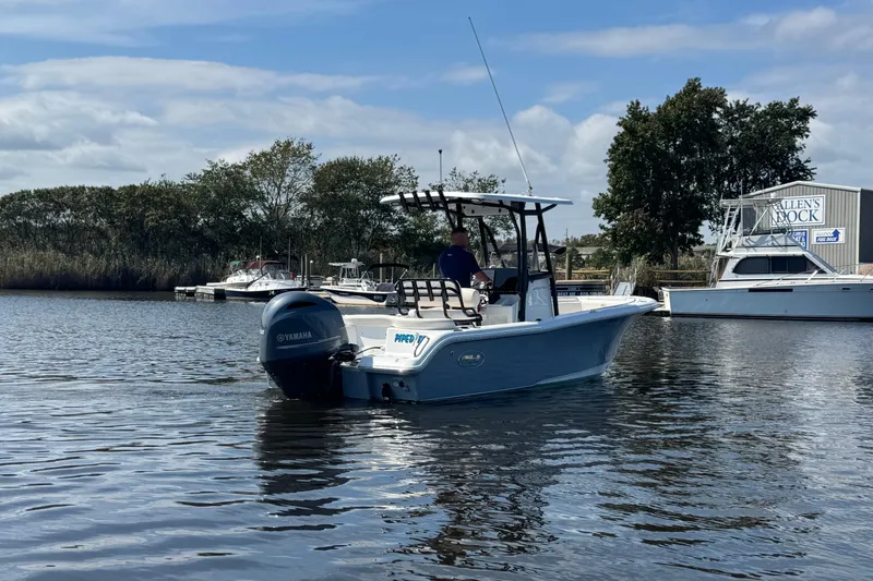 Slide: The Image of 2022 Sea Hunt Ultra 219 boat on calm water near a dock, with trees in the background. - 2
