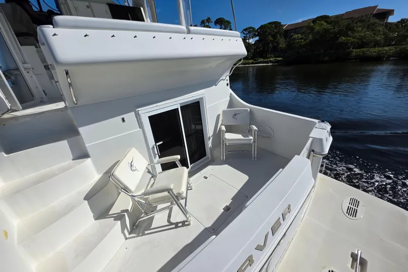 Slide: The Image of 2005 Carver 41 Cockpit Motor Yacht, spacious deck with chairs, near serene waterway. - 18
