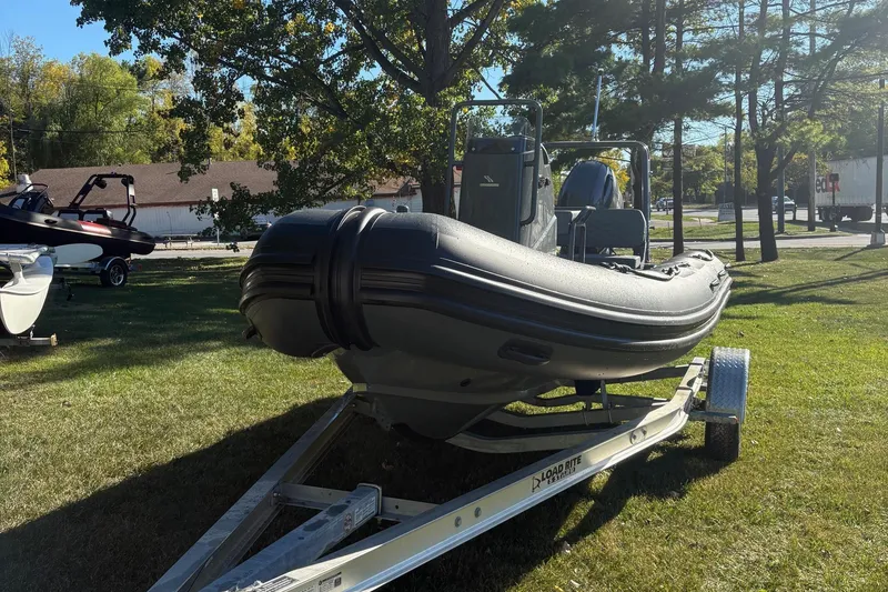 Slide: The Image of 2025 Highfield Patrol 500 boat on trailer, parked on grassy area with trees. - 2