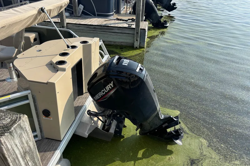 Slide: The Image of 2024 Godfrey SW2286FS pontoon boat with Mercury outboard motor docked on algae-covered water. - 2