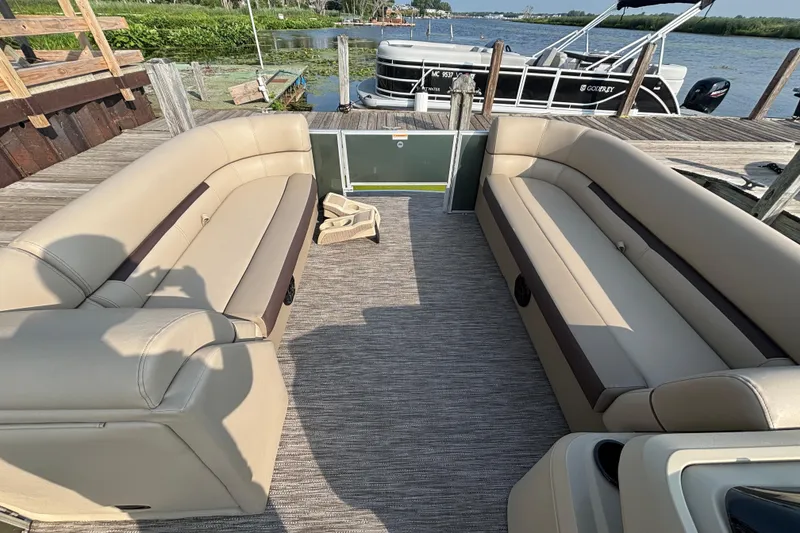 Slide: The Image of 2024 Godfrey SW2286FS pontoon boat interior with beige seating, docked by the water. - 7