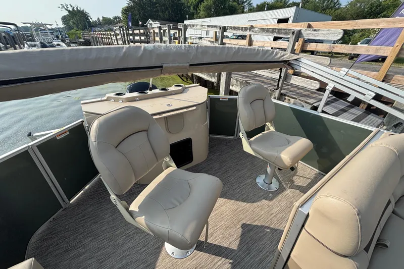 Slide: The Image of 2024 Godfrey SW2286FS boat interior with beige seating and helm, docked by water. - 9