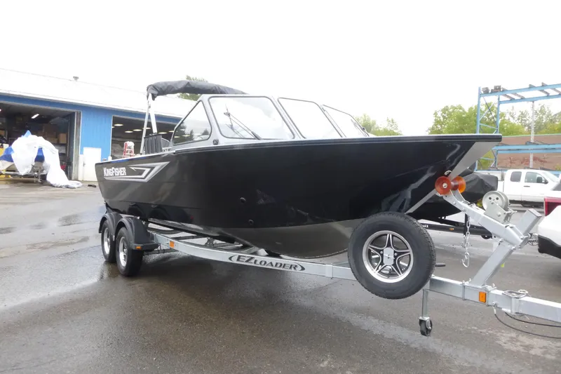 Slide: The Image of 2026 KingFisher 2025 Escape boat on trailer, parked outdoors near a blue building. - 4