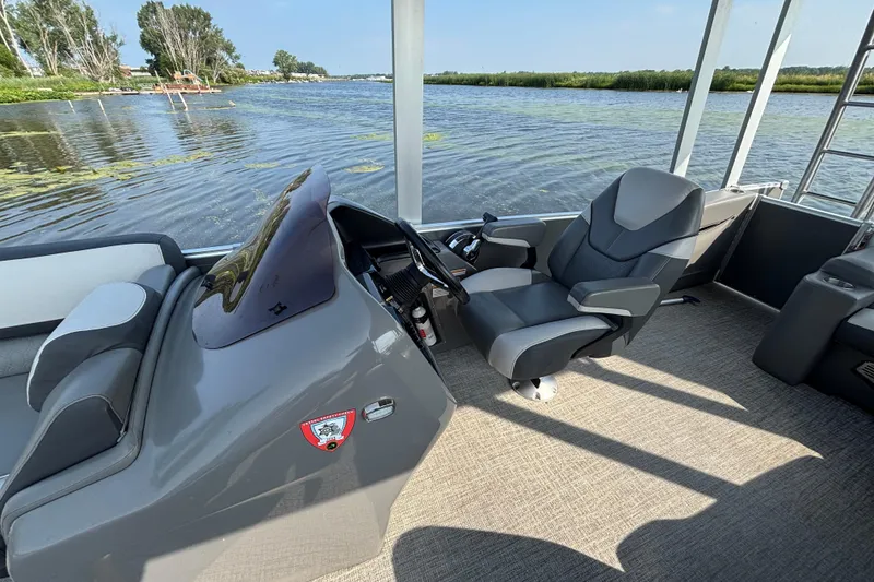 Slide: The Image of 2023 TAHOE AVALON Cascade boat interior with captain's chair and steering console on a lake. - 4