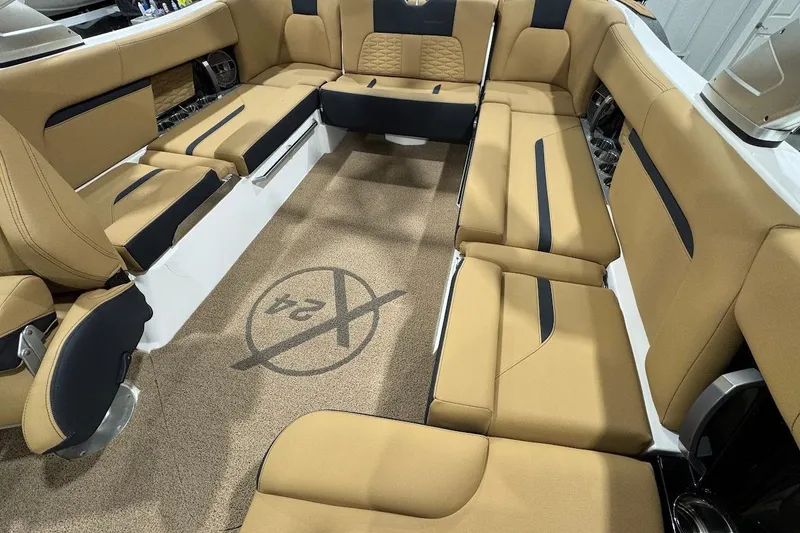 Slide: The Image of 2021 MasterCraft X24 boat interior with tan and black seating, featuring logo on carpet. - 11