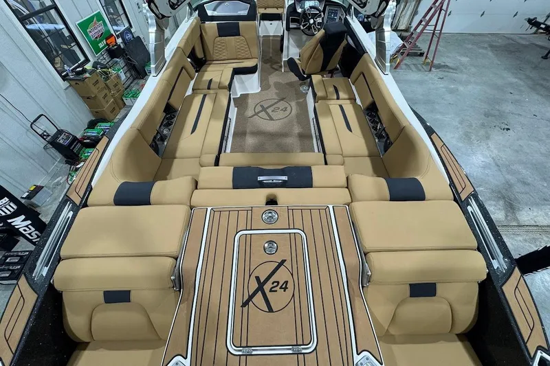 Slide: The Image of 2021 MasterCraft X24 boat interior with tan seating and wood accents in a garage setting. - 8