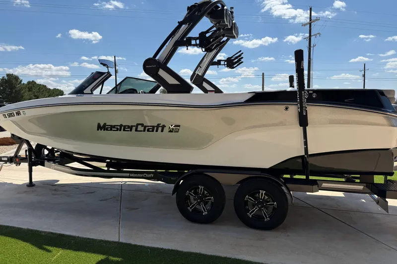Slide: The Image of 2023 MasterCraft XT24 boat on trailer, parked outdoors under a clear sky. - 7