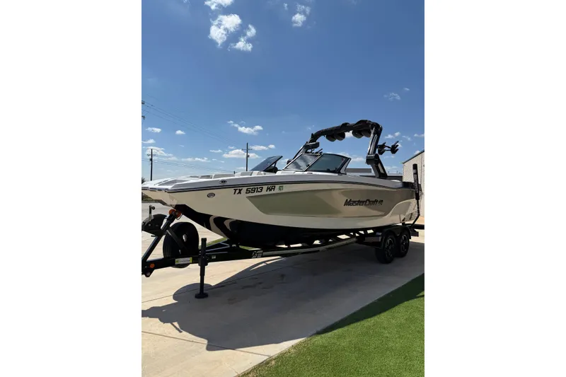 Slide: The Image of 2023 MasterCraft XT24 boat on trailer under clear blue sky. - 8