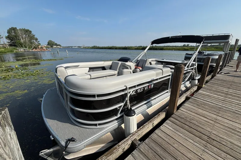 Slide: The Image of 2025 Godfrey SW2286MT pontoon boat docked on a sunny day by a wooden pier. - 2