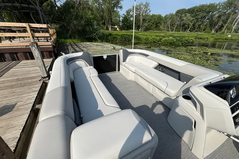 Slide: The Image of 2025 Godfrey SW2286MT pontoon boat interior with gray seating, docked by a lush lakeside. - 4