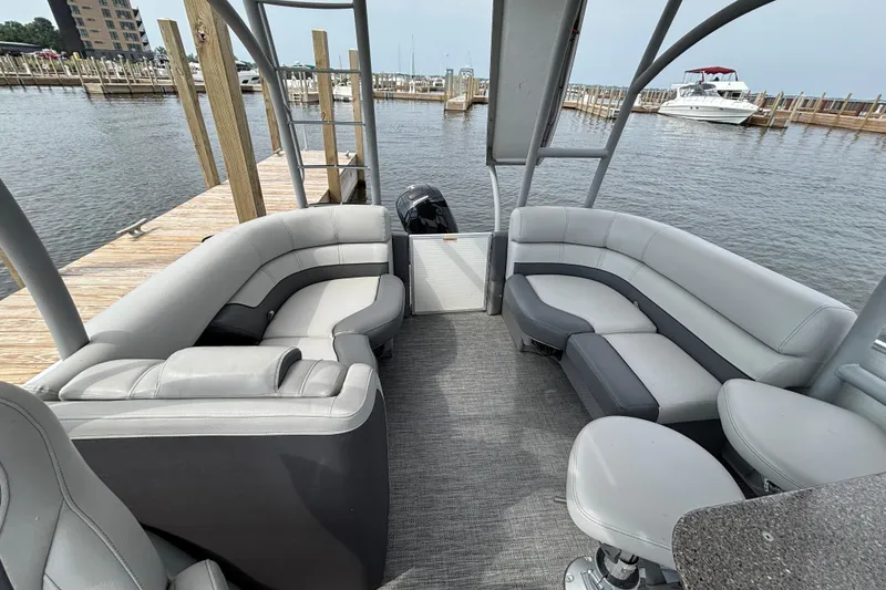 Slide: The Image of 2025 Godfrey MC235SDB pontoon boat interior with plush seating at a marina dock. - 10