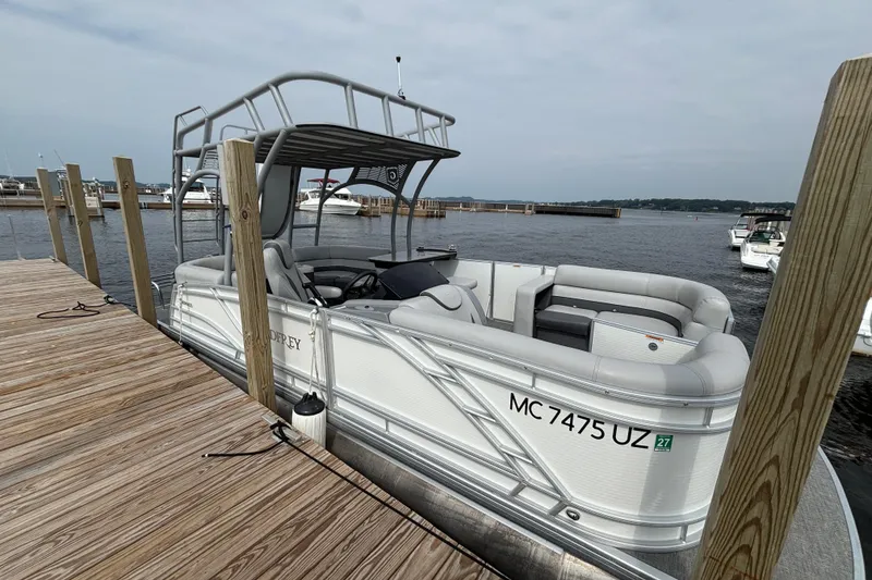 Slide: The Image of 2025 Godfrey MC235SDB pontoon boat docked at a marina, featuring spacious seating. - 2