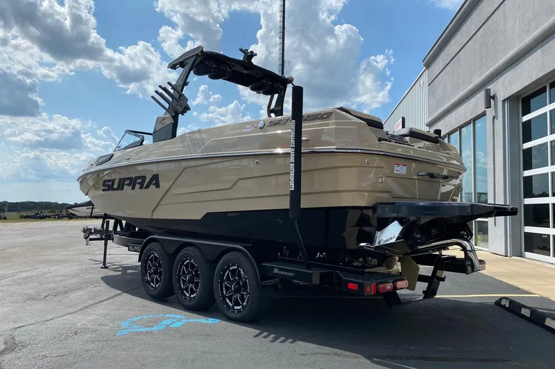 Slide: The Image of 2023 Supra SE450 boat on trailer, parked outside a building under a cloudy sky. - 2