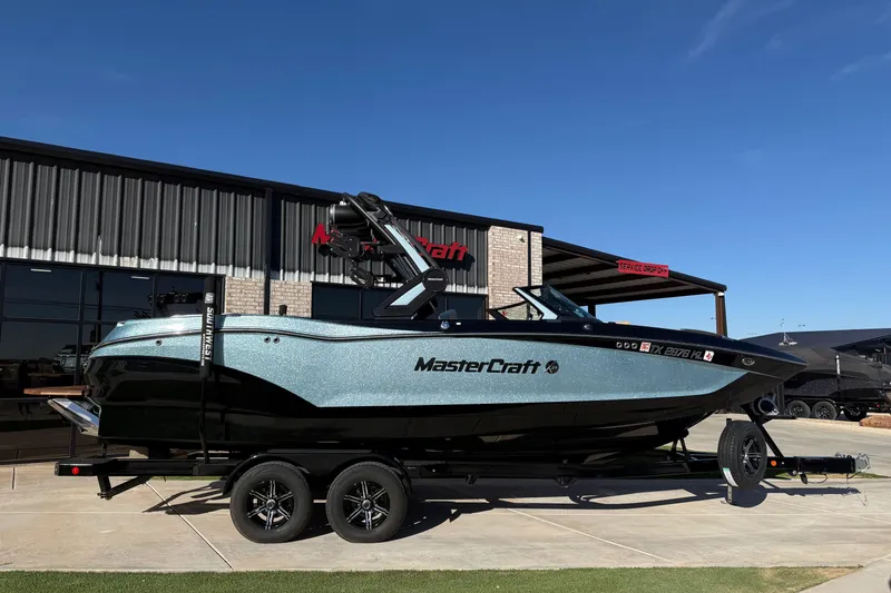 Slide: The Image of 2022 MasterCraft X24 boat on trailer outside dealership under clear blue sky. - 0