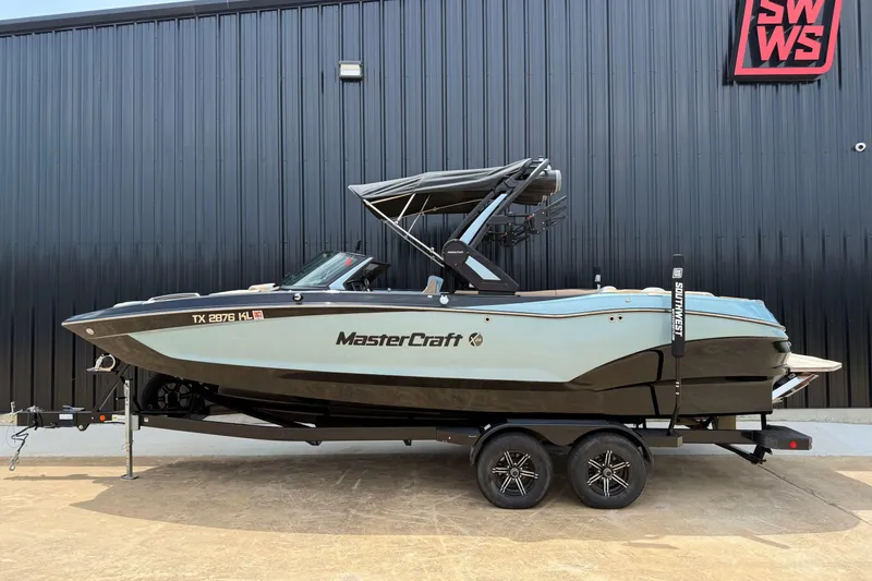 The Image of 2022 MasterCraft X24 boat on trailer, parked outside a black building. - 1