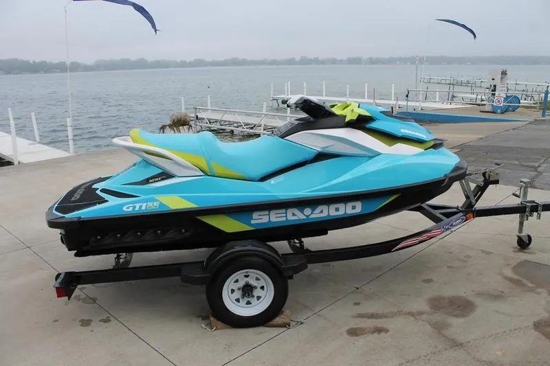 Slide: The Image of 2015 Sea-Doo GTI SE 155 jet ski on trailer by a lakeside dock. - 1