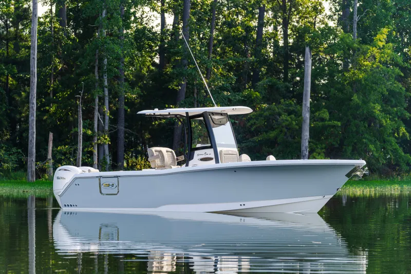 Slide: The Image of 2026 Sea Hunt Gamefish 25 boat on calm water, surrounded by lush trees. - 2