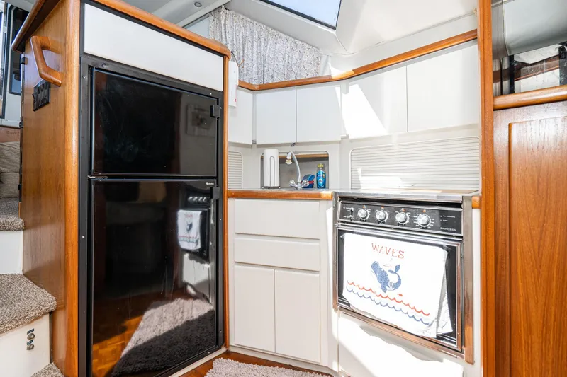 Slide: The Image of 1993 Carver 350 Aft Cabin Motor Yacht kitchen with stove, fridge, and wooden accents. - 14