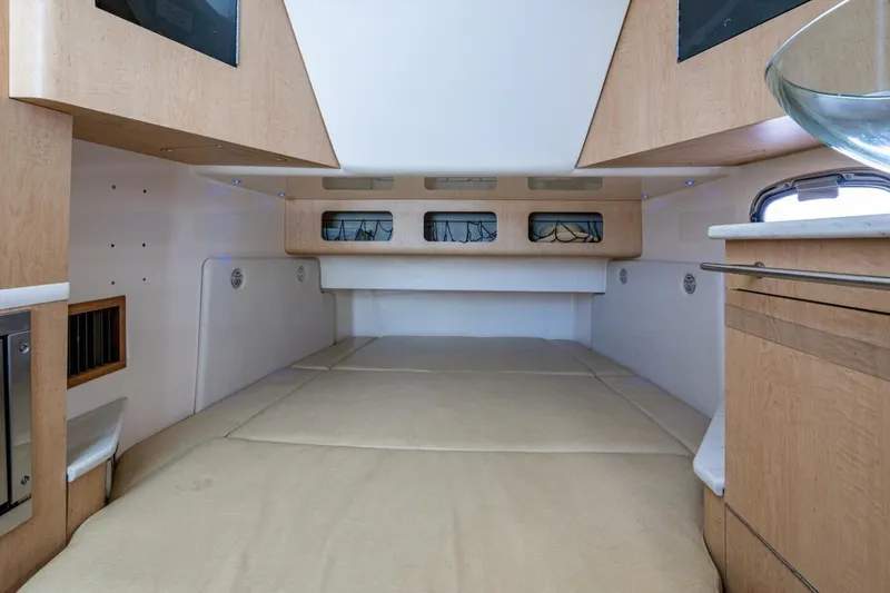 Slide: The Image of 2011 Boston Whaler 370 Outrage cabin interior with beige bedding and wooden cabinetry. - 12