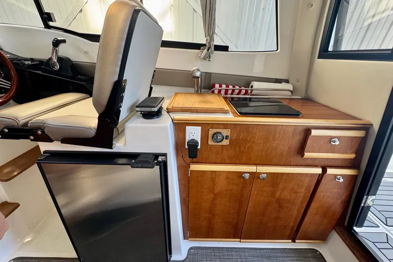 Slide: The Image of 2021 Cutwater C-24 Coupe interior with kitchenette, featuring stove, fridge, and wooden cabinetry. - 29
