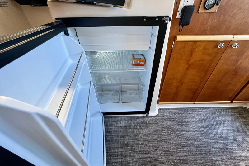 Slide: The Image of 2021 Cutwater C-24 Coupe interior with open refrigerator and wooden cabinetry. - 30