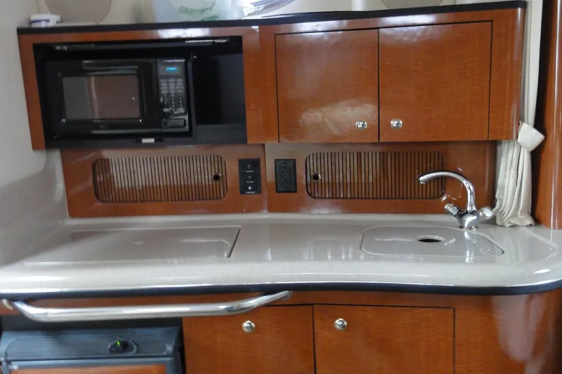 Slide: The Image of 2004 Sea Ray 320 Sundancer interior kitchen with microwave, sink, and wooden cabinetry. - 19
