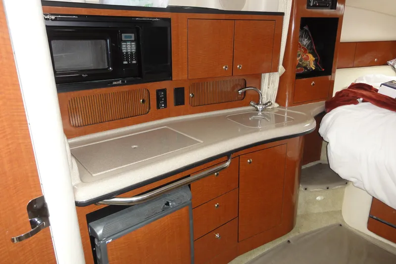 Slide: The Image of 2004 Sea Ray 320 Sundancer interior with kitchenette, featuring wood cabinets and a compact sink. - 22