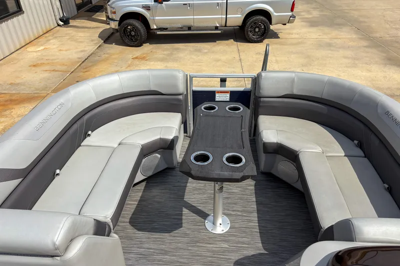 Slide: The Image of 2022 Bennington SX 22 pontoon boat interior with gray seating and table, parked near a truck. - 11
