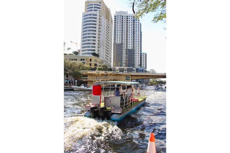 Slide: The Image of 2023 Maurell PONTOON boat cruising on urban waterway with city skyline backdrop. - 4